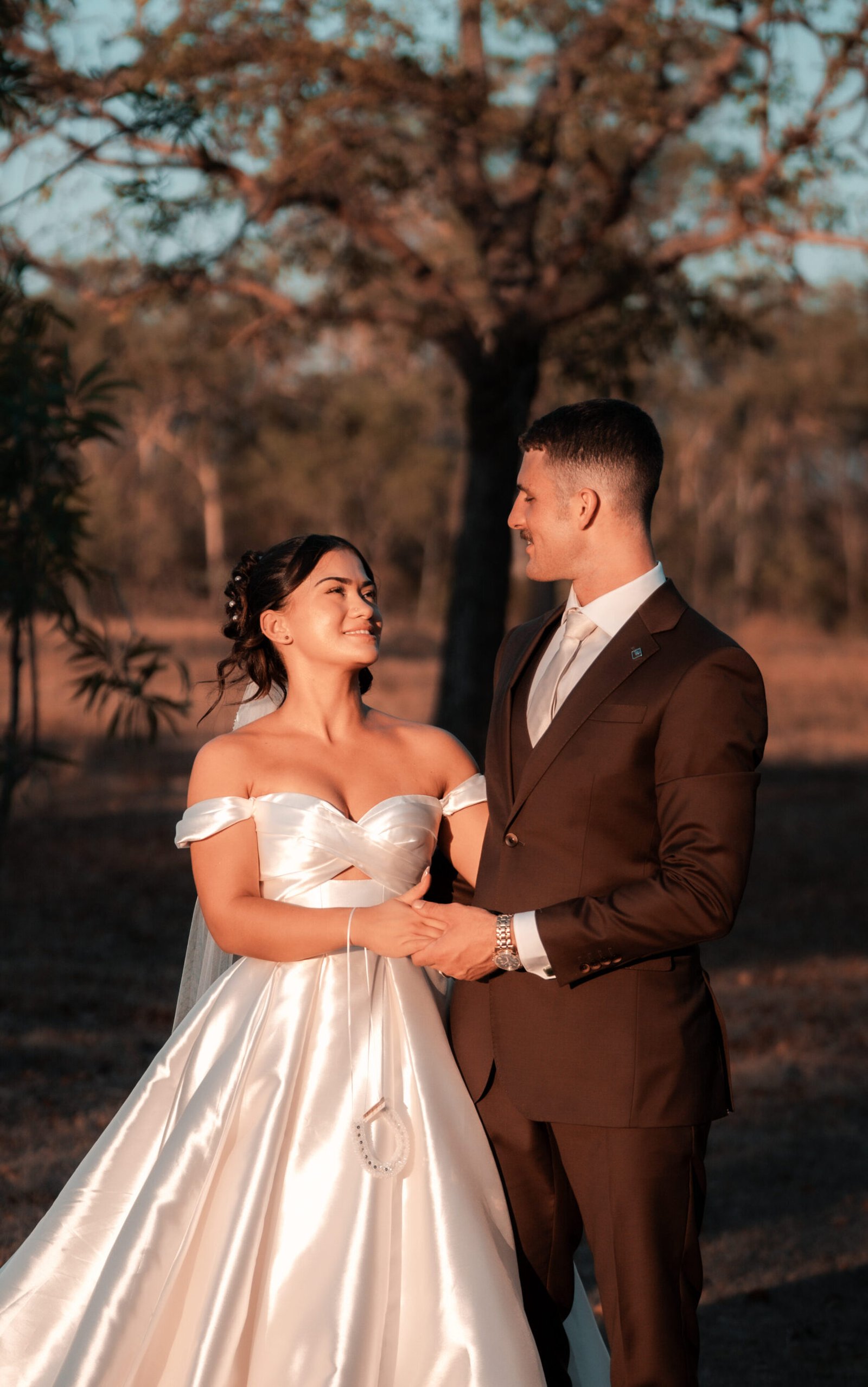 Post wedding shoot of a couple - the bride wearing a white gown and the groom wearing a dark brown suit with a territory outback background.